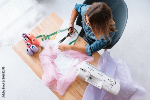 Hands mistress seamstress made a beautiful bright fashionable clothes. The crosslinking parts of the pattern. Work place. Top view. Light Textile industry creative moments photo