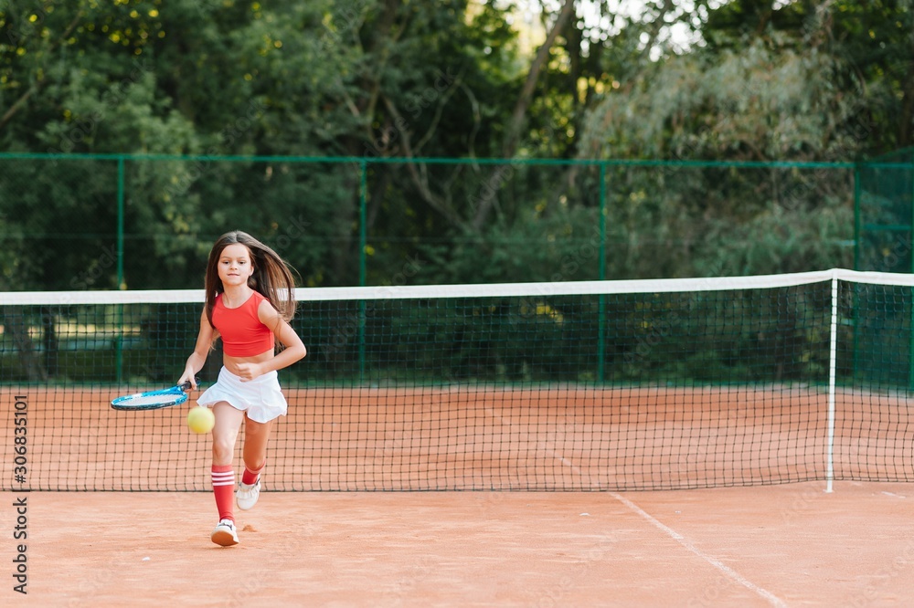 Child playing tennis on outdoor court. Little girl with tennis racket and ball in sport club. Active exercise for kids. Summer activities for children. Training for young kid. Child learning to play