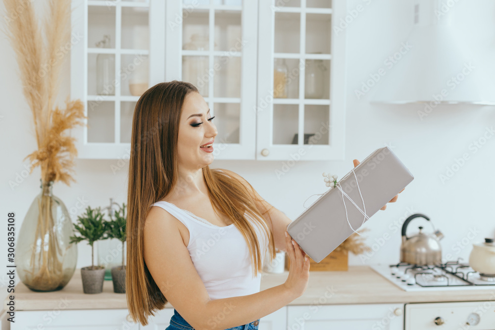 Beautiful young woman holds New Year present in modern bright Scandinavian kitchen Beautiful young woman holds New Year present in modern bright Scandinavian kitchen