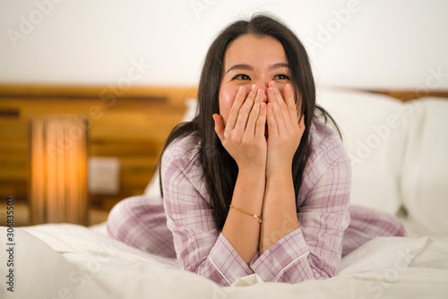 lifestyle portrait of young beautiful and sweet Asian Chinese woman in bed feeling happy and relaxed wearing cute pajamas enjoying lazy Sunday morning at home