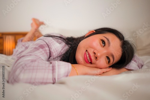 lifestyle portrait of young beautiful and sweet Asian Chinese woman in bed feeling happy and relaxed wearing cute pajamas enjoying lazy Sunday morning at home