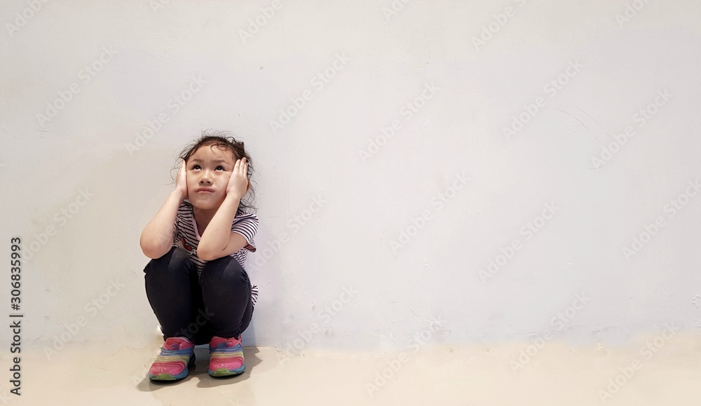 Sad little girl sitting against the wall in despair Sad little girl sitting against the wall in despair
