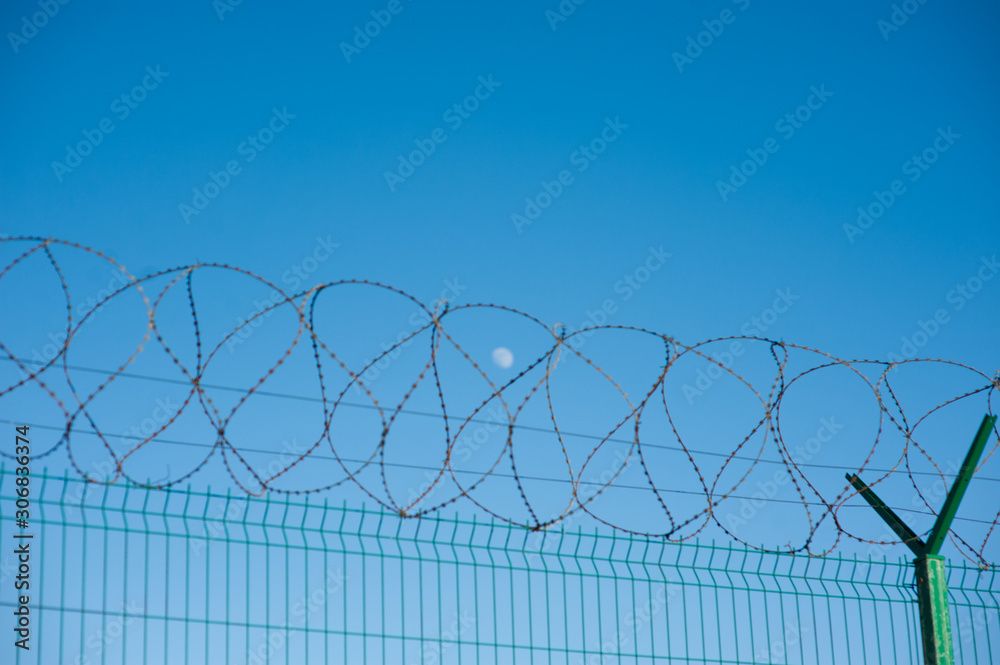 prison concentration outdoor camp concept of barbed razor wire on fence with blue sky with moon on background prison concentration outdoor camp concept of barbed razor wire on fence with blue sky with moon on background