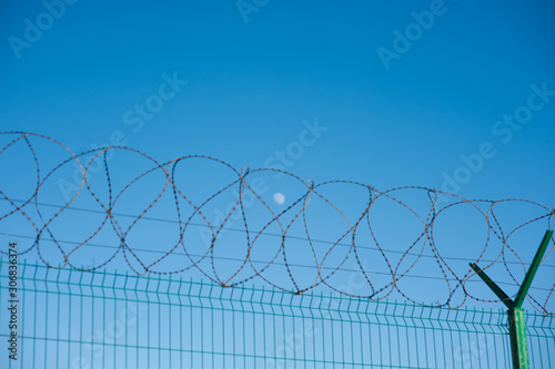 prison concentration outdoor camp concept of barbed razor wire on fence with blue sky with moon on background