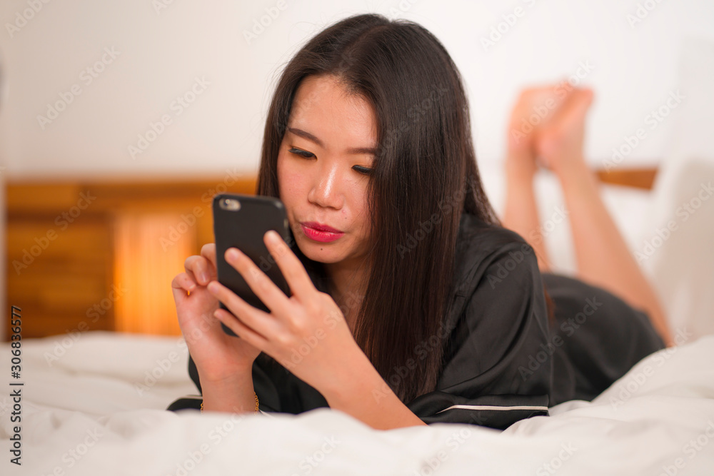 young beautiful and sweet Asian Chinese woman in cute nightgown playful in bed using mobile phone enjoying social media or online dating app happy and relaxed young beautiful and sweet Asian Chinese woman in cute nightgown playful in bed using mobile phone enjoying social media or online dating app happy and relaxed