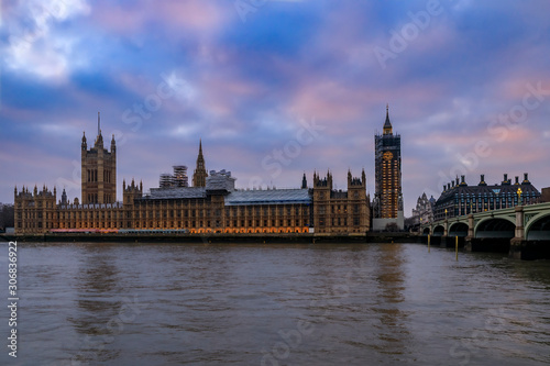 Westminster Palace and Big Ben covered in scaffolding for restoration viewed across the Thames at sunset in London, UK