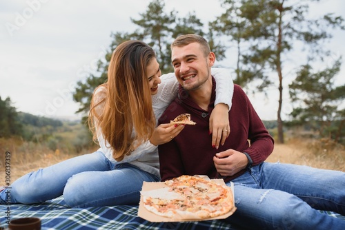 Couple in love lying on a picnic blanket in a park, enjoying beautiful autumn day in nature and cuddling