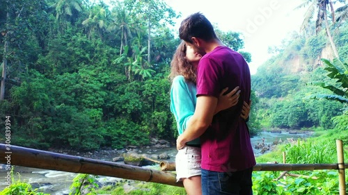 Young couple adoring and kissing each other on a beautiful tropical forest with lush vegetation and palm trees around a river valley in Thailand