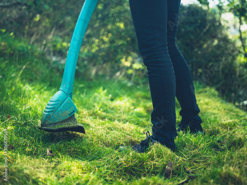 Young woman cutting grass with a strimmer