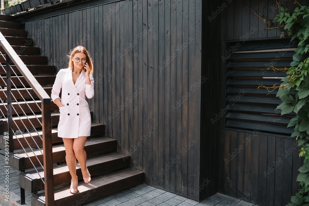 Smiling businesswoman dressed in formal wear having pleasant conversation on mobile phone with friend, happy attractive female speaking on cell telephone while resting in office interior after work