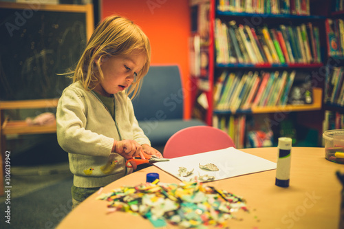 Toddler using scissors and glue at school photo