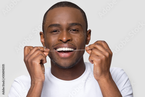 Happy African American man with healthy smile using dental floss
