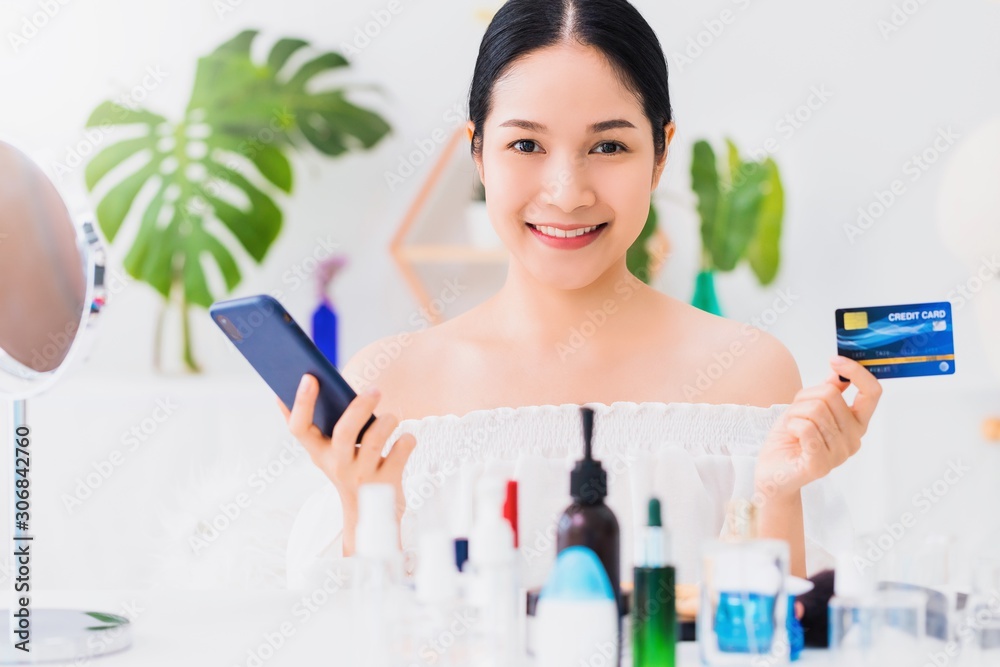 Asian beautiful woman using smartphone with credit card shopping online at home with cosmetic.Convenience in buying online products with modern business technology concept. Asian beautiful woman using smartphone with credit card shopping online at home with cosmetic.Convenience in buying online products with modern business technology concept.