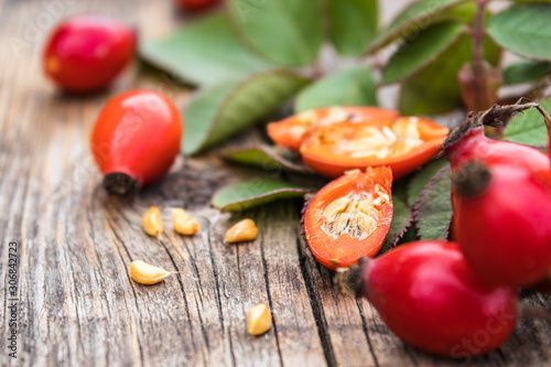 Fresh red rose hips and ripened berries in half with seeds on a wooden table.