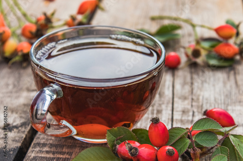 Tea or tincture with rose hips in a glass cup near red berries on a wooden table.