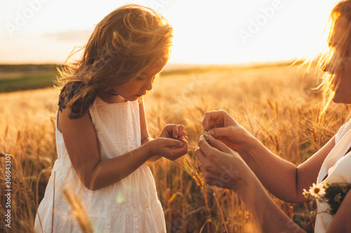 Foto Lovely little girl holding wheat grain with her mother in a field of wheat against sunset