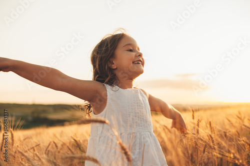 Beautiful little girl laughing and running with hand up in a wheat field against sunset. Freedom concept. photo