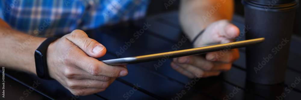 Focus on male hands holding modern tablet and sitting at wooden table in brewery. Guy chatting with fiends via special internet app. Electronic technology concept. Blurred background