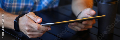 Focus on male hands holding modern tablet and sitting at wooden table in brewery. Guy chatting with fiends via special internet app. Electronic technology concept. Blurred background