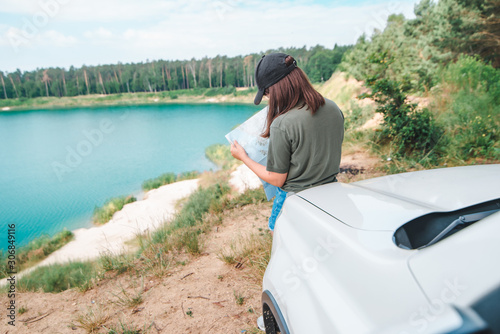 woman checking with map on the suv car hood lake with blue water on background © phpetrunina14