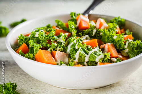 Kale and baked sweet potato salad with tahini dressing in white bowl. Healthy vegan food concept.