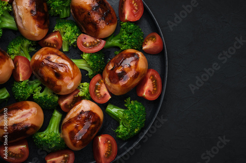 grilled sausages with tomatoes,  broccoli on black plate. dark background top view