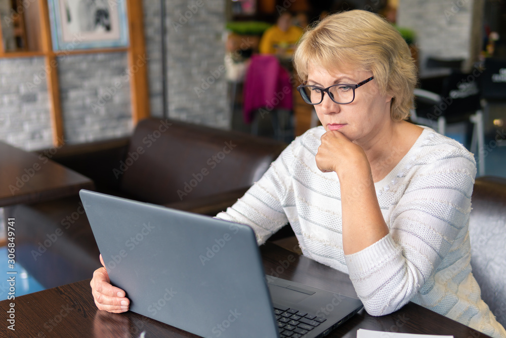 A woman with a laptop looks at a document in a cafe, office A woman with a laptop looks at a document in a cafe, office