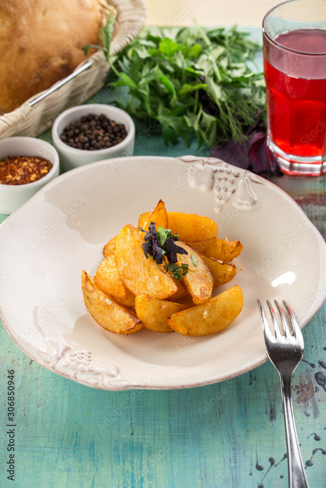 Baked potato wedges on white plate with glass of red drink on blue wooden table Baked potato wedges on white plate with glass of red drink on blue wooden table