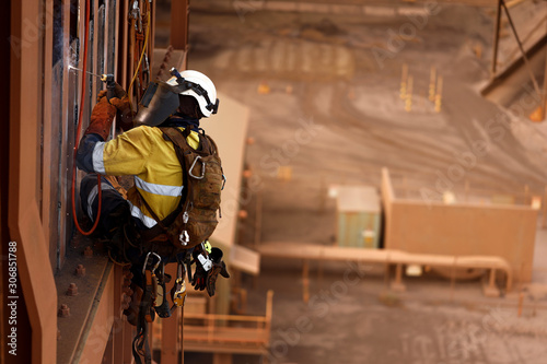 Close up shoot of rope access stick welder wearing full body safety harness equipment, abseiling working at height conducting welding chute parent repairs on construction site Perth, Australia