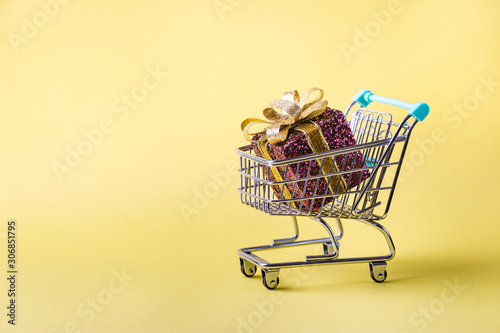 shopping cart full of christmas presents on bright yellow background