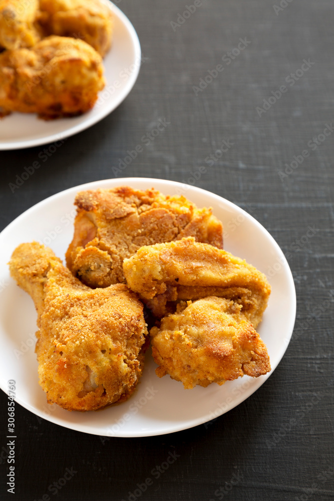 Delicious homemade oven baked fried chicken on a white plate over black background, low angle view. Copy space.