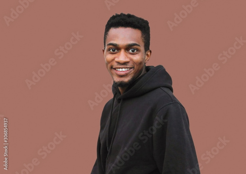 Portrait young smiling african man looking at camera wearing black hoodie isolated on brown background