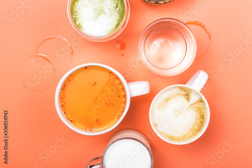 Different drinks cappuccino, tea, sea buckthorn juice, milk, water, orange juice and matcha on a bright coral pink background. Top view, flat lay.