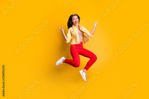 Full length body size turned photo of cheerful shouting woman showing horned fingers rock sign in red pants wearing white shoes isolated vivid color background