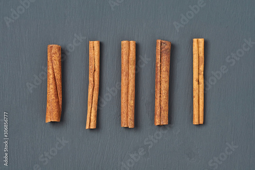 Row of five flavour cinnamon sticks lies on dark scratched desk on kitchen. Top view. Close-up