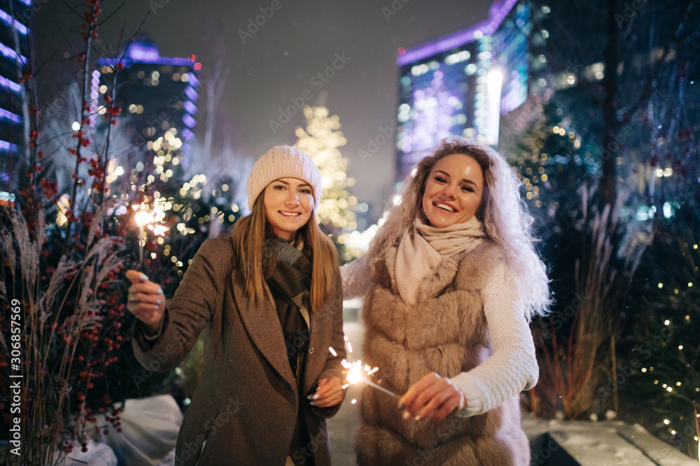 Photo of two women with Bengal lights on winter walk on background of decorated spruce