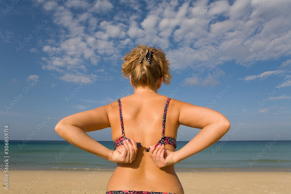 Slender natural blonde takes off her bra on the beach. Stock Photo