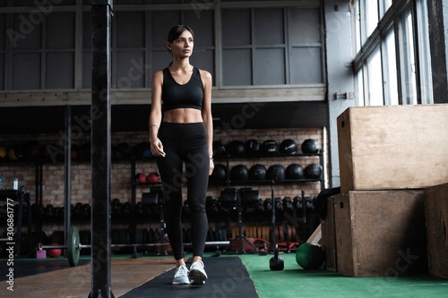 Shot of strong woman standing in crossfit gym and looking away. Confident fitness female model in sportswear.