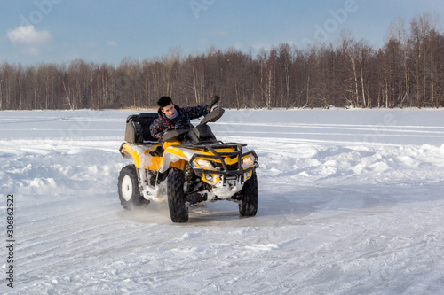 Young man rides ATV on ice on snow frozen lake in cold sunny winter day.