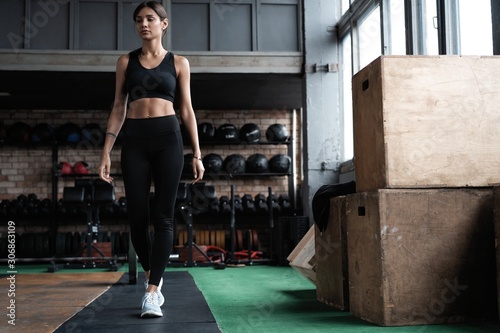 Shot of strong woman standing in crossfit gym and looking away. Confident fitness female model in sportswear. © opolja