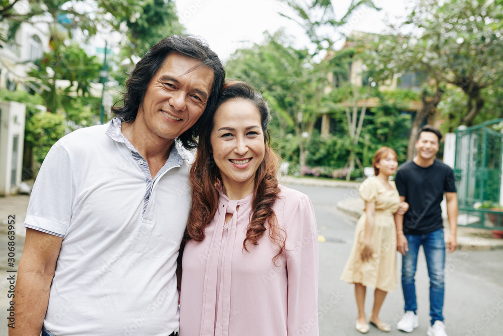 Portrait of mature hugging Asian couple, thait adult children standing in background Portrait of mature hugging Asian couple, thait adult children standing in background