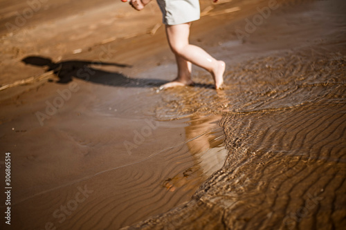 Fototapeta Naklejka Na Ścianę i Meble -  Small vawes of baltic sea. Patterns of water and light. People in background. Kid walking in water. 