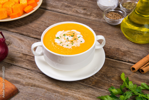 Pumpkin soup in a white soup cup on a old rustic wooden table. Selected focus