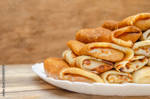 Pancakes with filling stacked pyramid on a white plate, standing on a wooden background close-up
