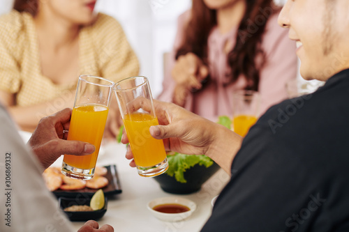 Cropped image of smiling guests clinking glasses of fruit juice at dinner
