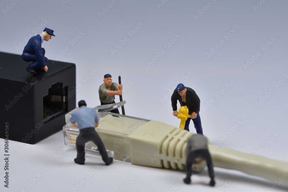 Fototapeta premium Mini workers are trying to fit a nethernet plug in a connector