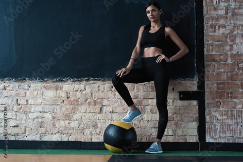 Sportive caucasian cross fit woman with fitness ball stand in gym, look at camera photo