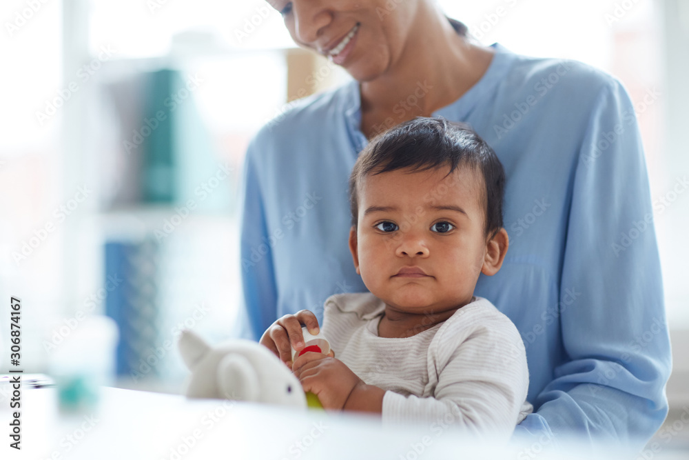 Portrait of cute baby boy sitting on mother's knees looking at camera and playing toys Portrait of cute baby boy sitting on mother's knees looking at camera and playing toys
