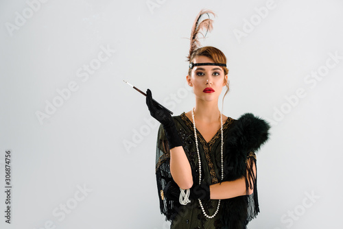 stylish woman with cigarette holder looking at camera isolated on grey