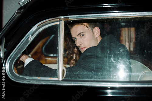 handsome and dangerous man looking at camera while sitting in car